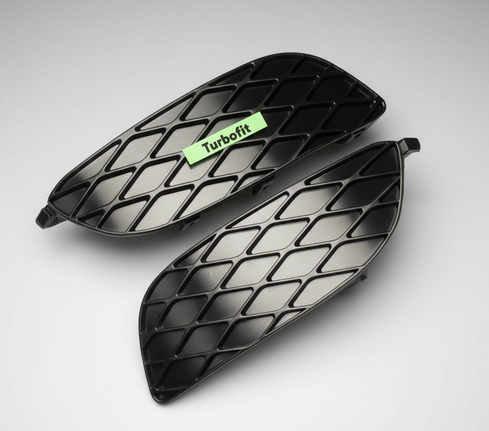 Two black car air vent covers with a green Audi logo on a wooden surface.