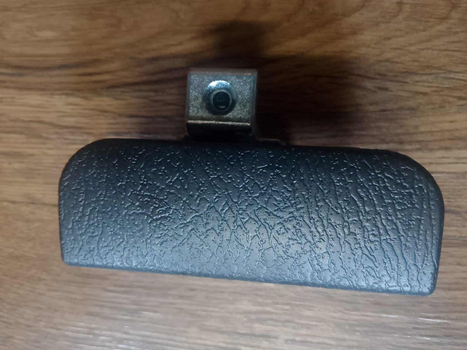 Black textured object with a metallic clip on a wooden surface