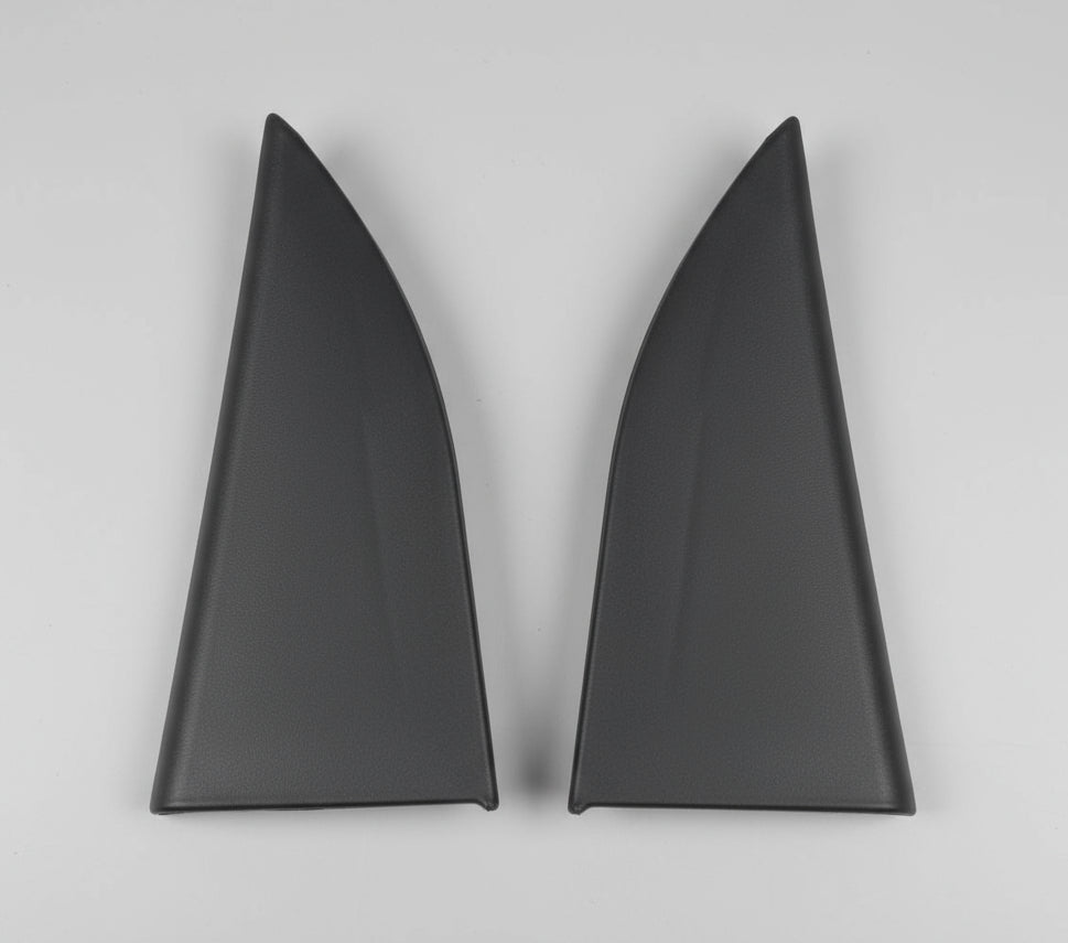 Two black triangular car parts on a cardboard surface.