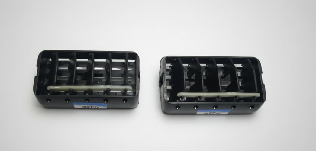 Two black plastic connectors on a white surface with a grid pattern.