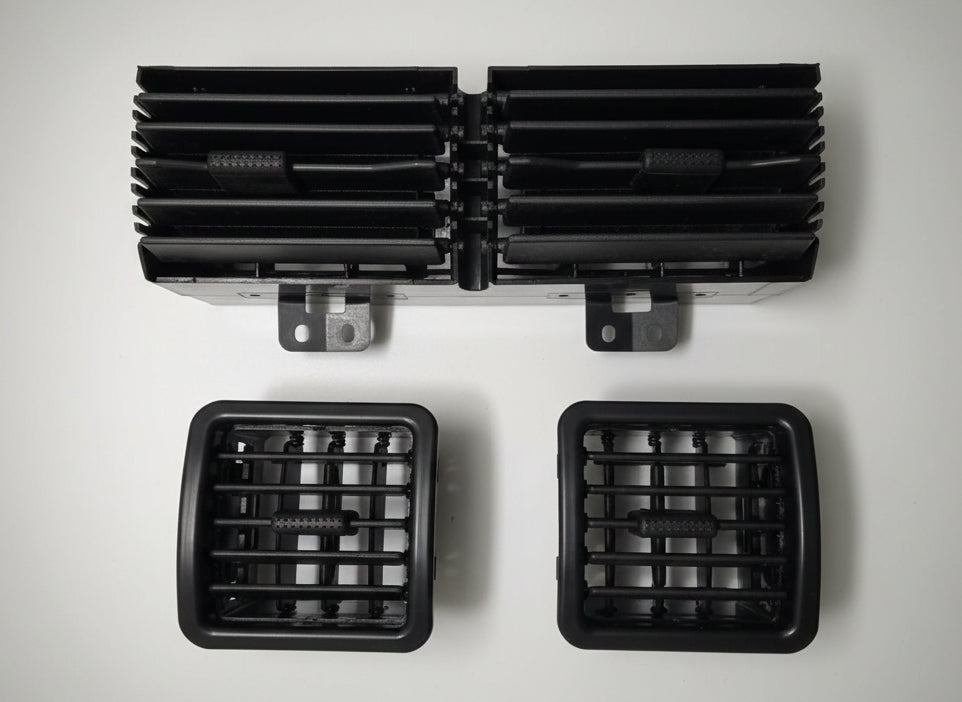 Two black automotive air vents on a white surface with a grid pattern.