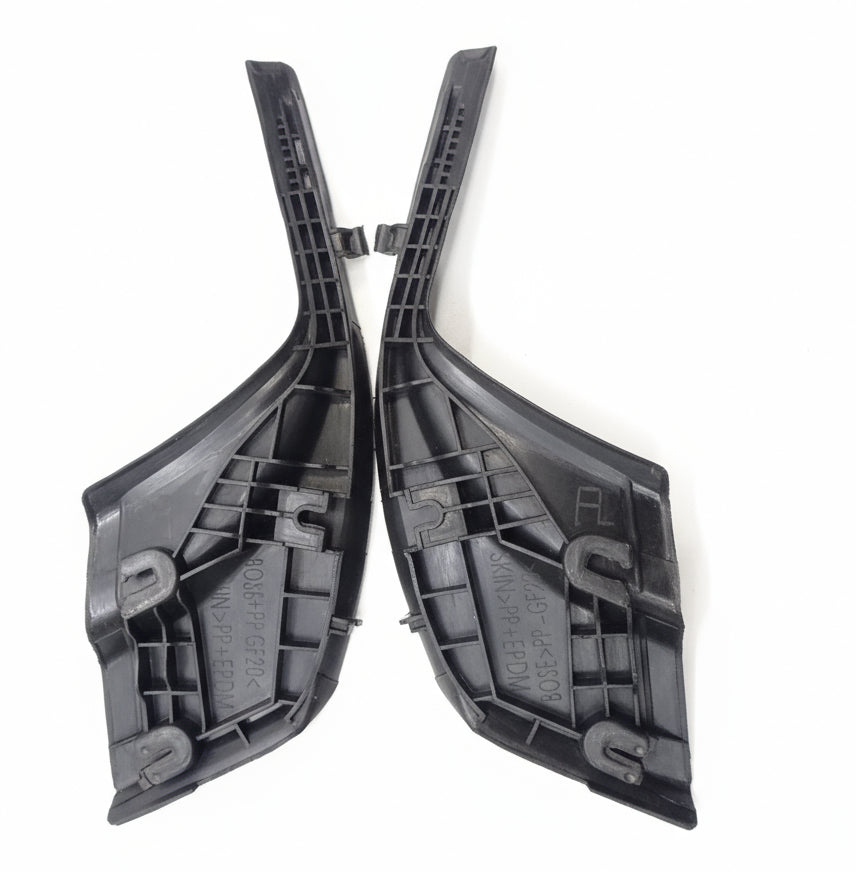 Two black plastic car parts on a scratched metal surface