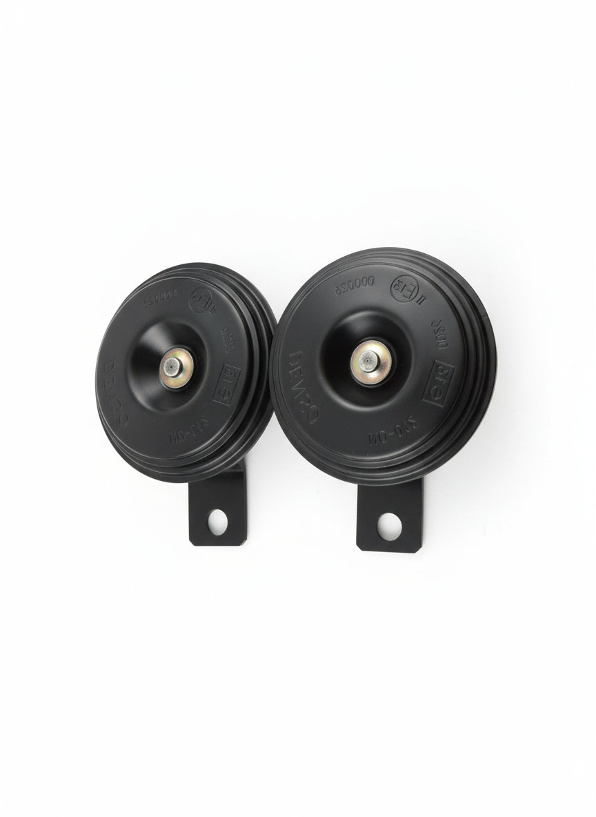 Two Denso car horns on a white square piece of paper with a wooden background