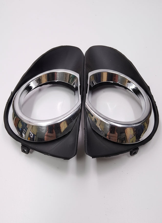 Two car fog lights with black casings and chrome centers on a white surface.