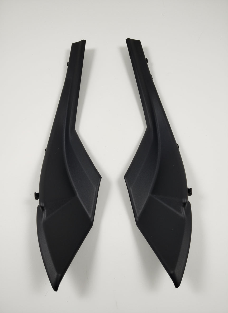 Two black plastic car parts on a light gray floor.