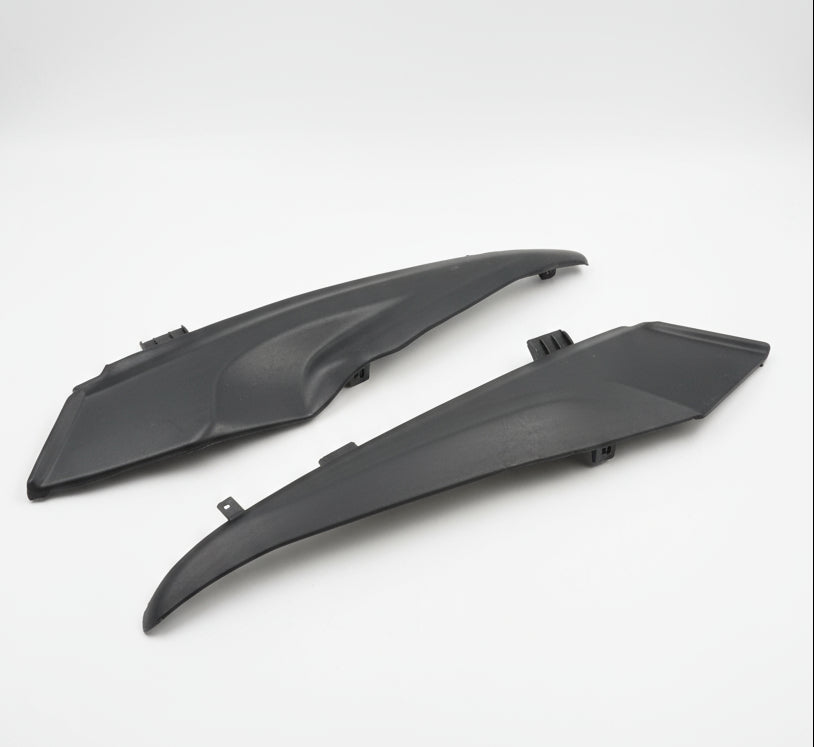 Two black plastic car parts on a textured white surface